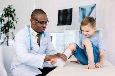 A male doctor treats the broken leg of a boy